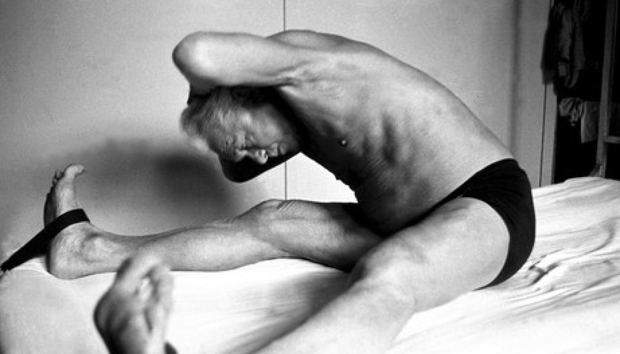 Ein Originalbild von Joseph Pilates wie er auf einem Bett eine Dehnübung ausübt