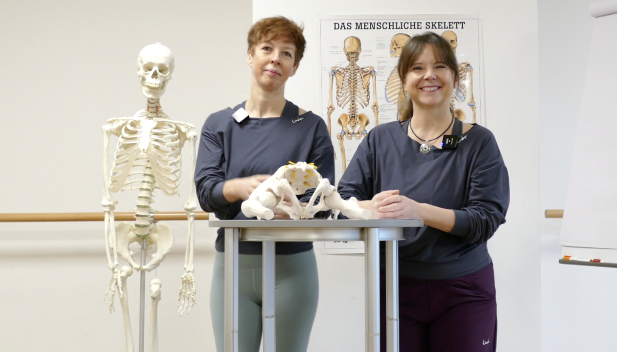 Kerstin Bredehorn und Jenni Bergunde stehen an einem Stehtisch, darauf ein knöchernes Beckenmodell.