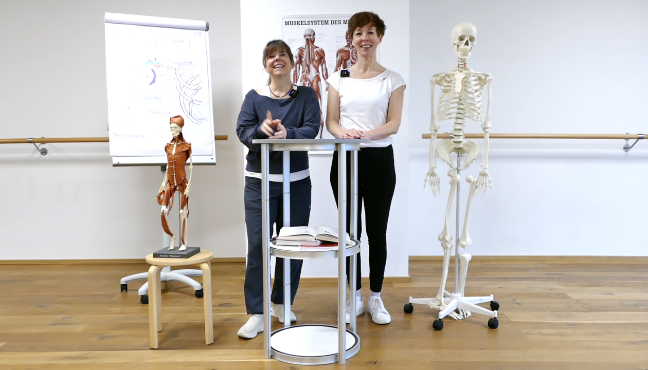 Kerstin Bredehorn und Jenni Bergunde stehen hinter einem Stehtisch, rechts ein Skelett, links ein kleines Skelett mit gekneteten Muskeln